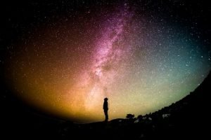 A woman is standing under the milky in the night sky, embarking on a spiritual journey while embracing the beauty of ageing well.