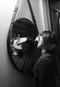 A black and white photo of a woman lacking confidence in front of a mirror.