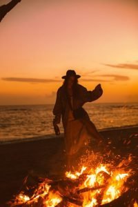 A wise woman gracefully dancing around a bonfire on the beach.