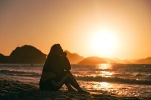 A wise woman sitting on the beach at sunset, contemplating her regrets in midlife.