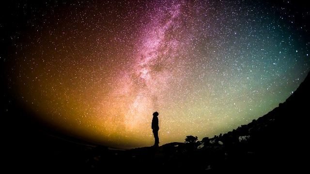A woman is standing under a vibrant and ethereal Milky Way in the night sky, embarking on a spiritual journey.